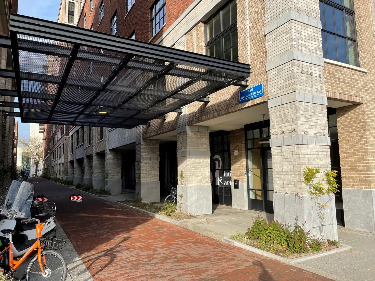 Ingang van een modern appartementencomplex aan de Karl Weisbardstraat met een overkapping en geparkeerde fietsen.